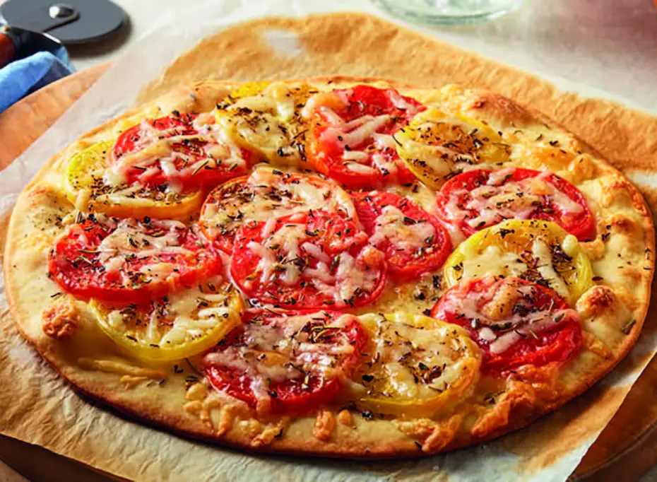 Pizza garnie de tomates fraîches, fromage et herbes, préparée avec des ingrédients de qualité par Cérélia.