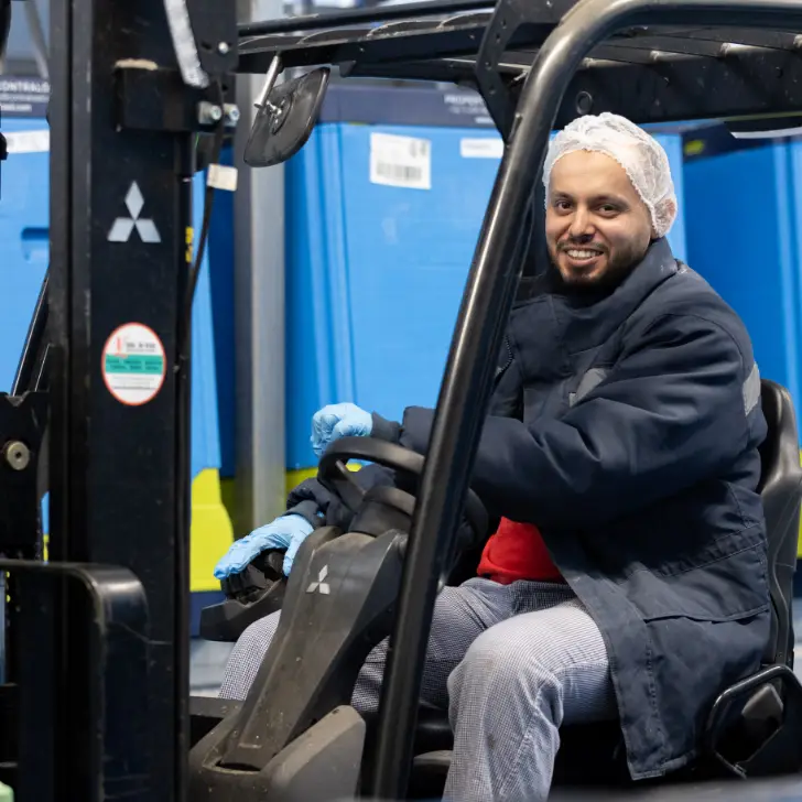 Un cariste souriant conduisant un chariot élévateur dans l'entrepôt de Cérélia